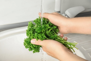 Woman washing fresh parsley under tap water in kitchen sink, closeup