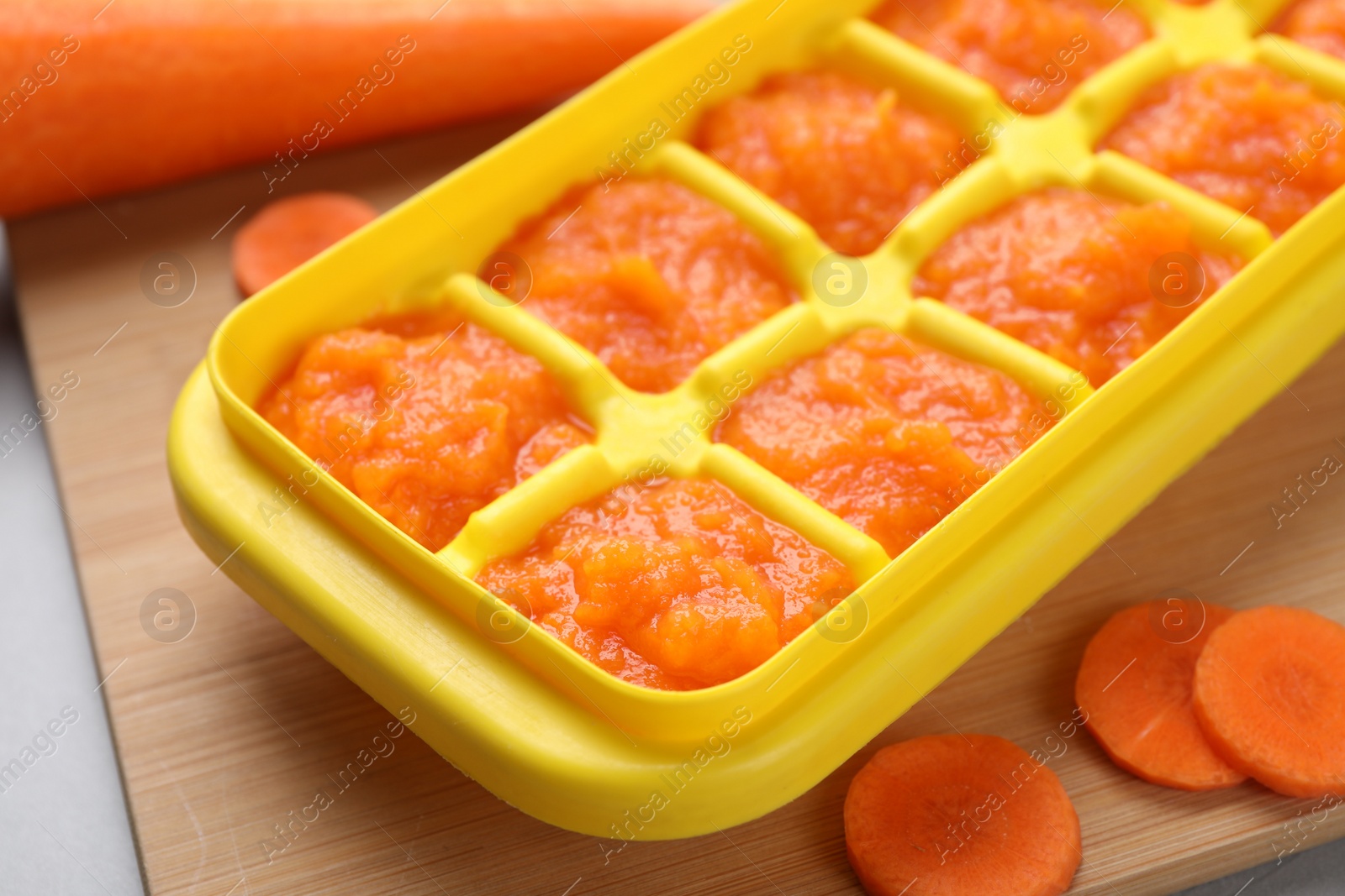 Photo of Carrot puree in ice cube tray on wooden board, closeup. Ready for freezing