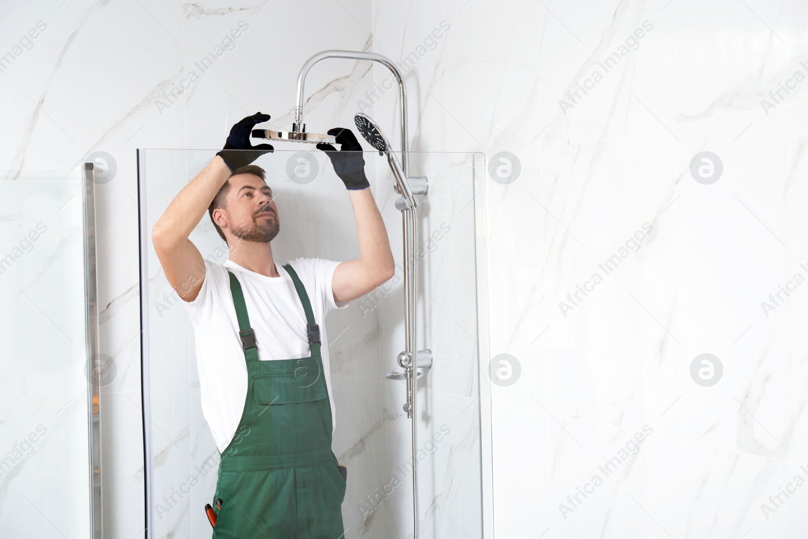 Photo of Professional handyman working in shower booth indoors, space for text