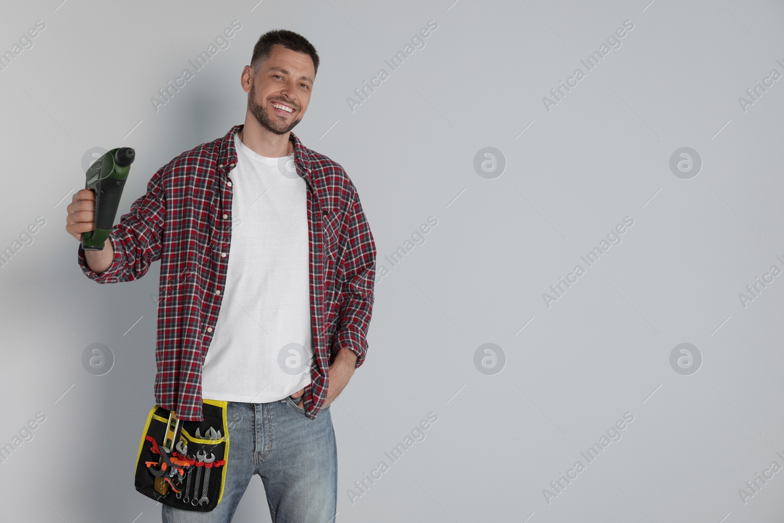Photo of Handsome worker with electric drill on white background, space for text