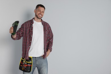 Handsome worker with electric drill on white background, space for text