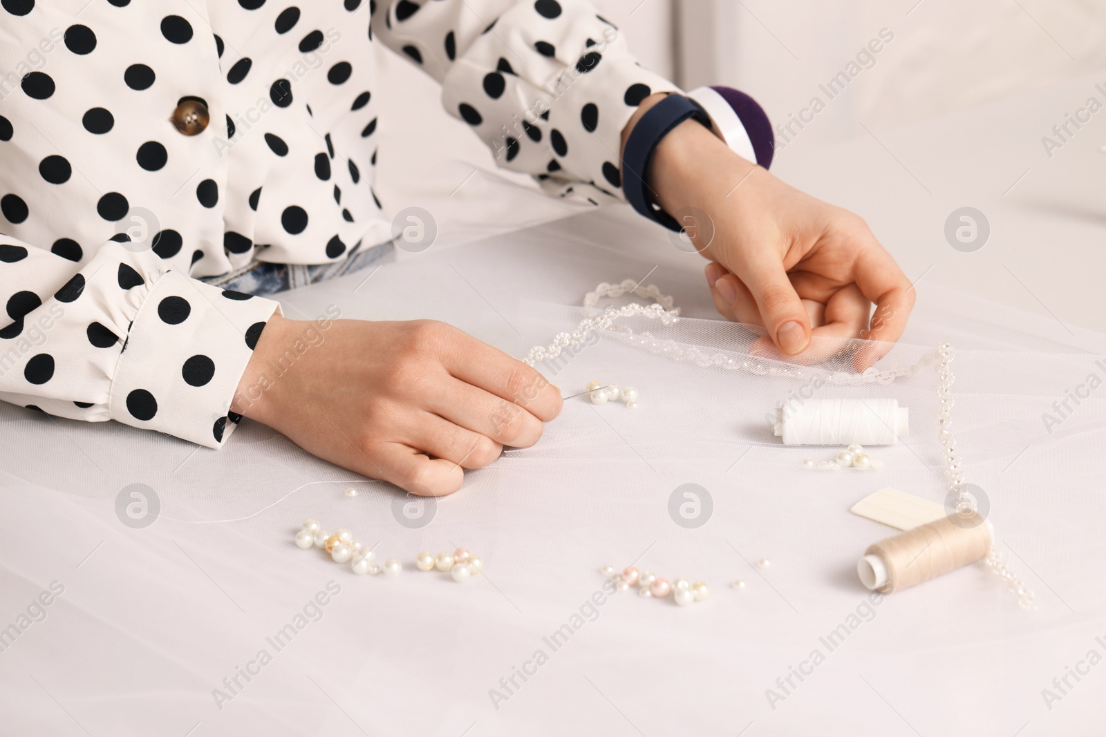 Photo of Dressmaker with sewing accessories at white table in atelier, closeup