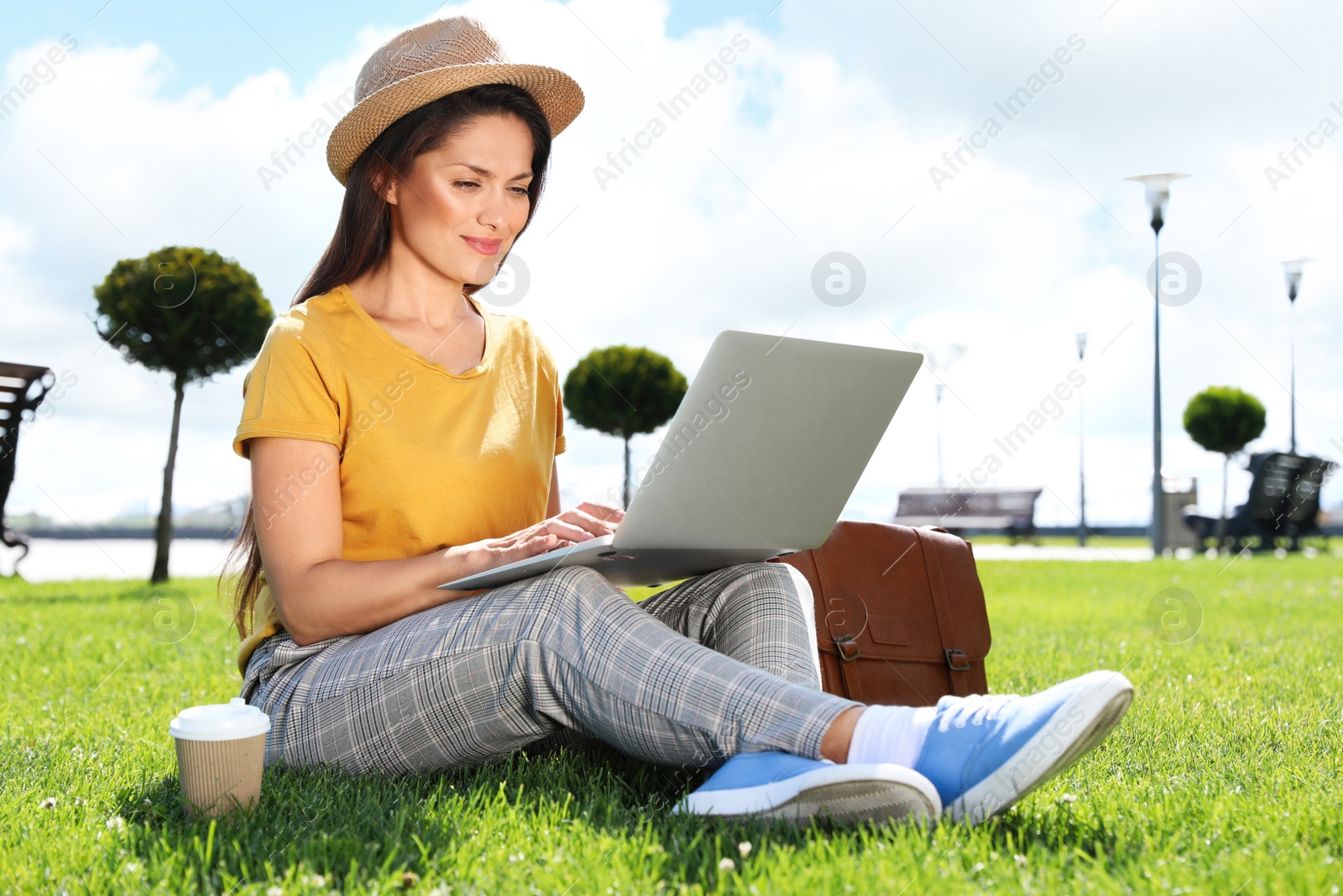 Photo of Beautiful woman with laptop sitting on green lawn outdoors