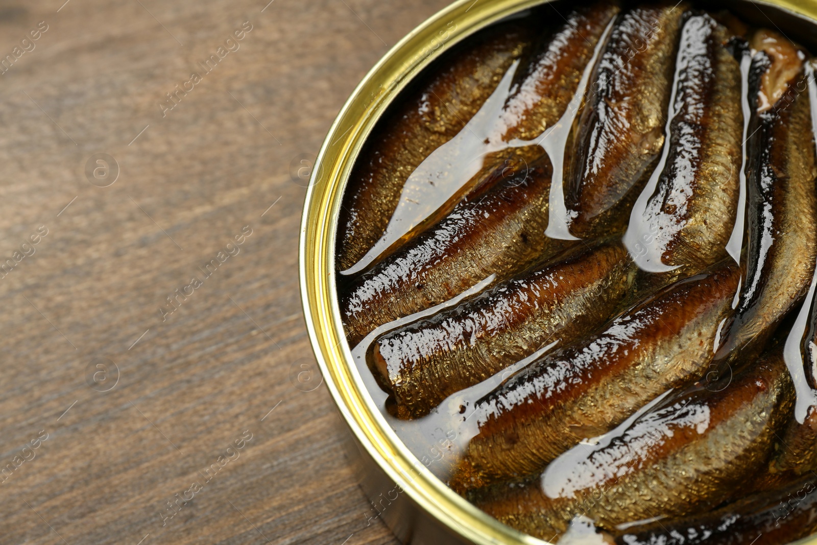 Photo of Sprats in tin can on wooden table, closeup. Space for text