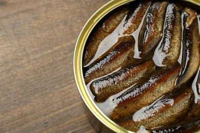 Photo of Sprats in tin can on wooden table, closeup. Space for text