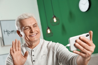 Photo of Mature man using video chat on mobile phone at home