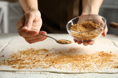 Woman pouring brown sugar onto dough while making pie at table, closeup