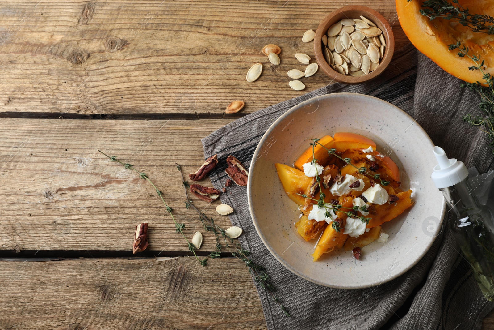 Photo of Baked pumpkin slices served with cheese, thyme and pecans on wooden table, flat lay. Space for text
