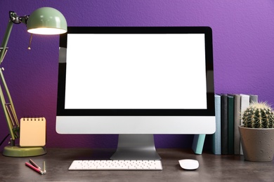 Photo of Comfortable workplace with modern computer and cactus on table near purple wall. Space for design