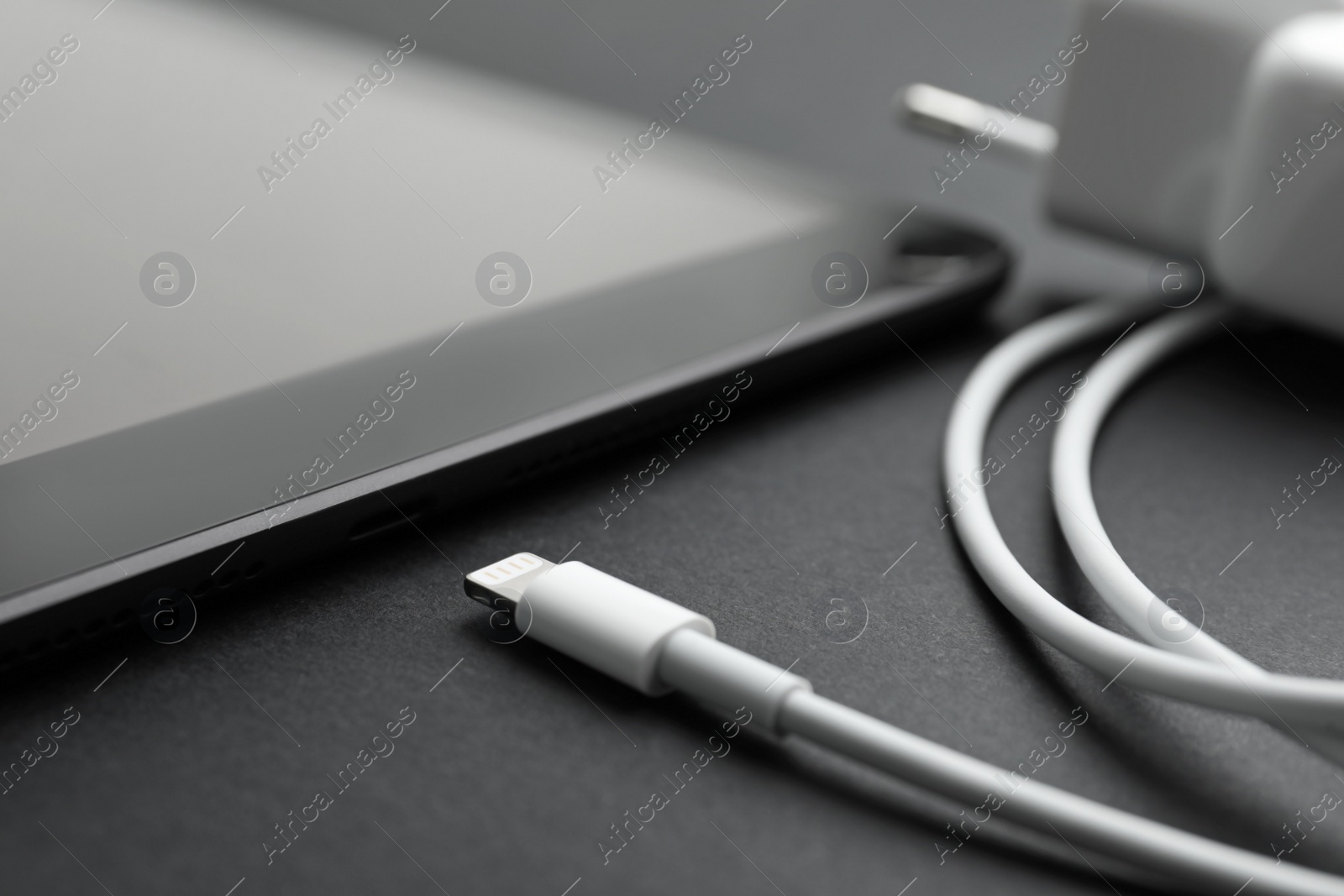 Photo of Tablet and USB charge cable on black background, closeup. Modern technology