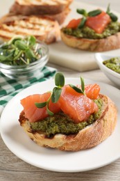 Delicious bruschetta with salmon and pesto sauce on wooden table