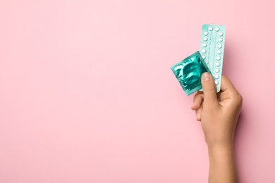 Photo of Woman holding condom and birth control pills on pink background, top view with space for text. Safe sex