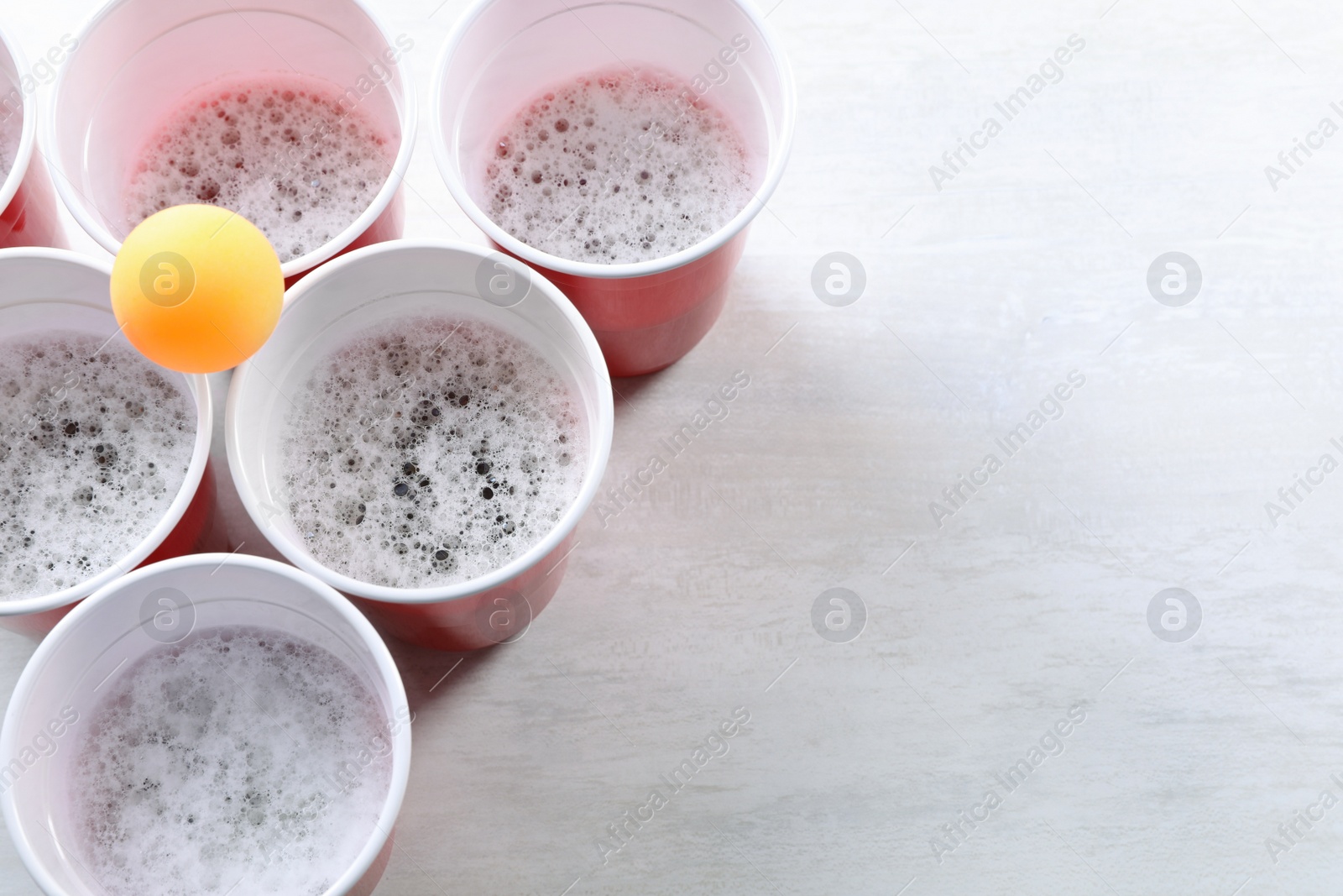 Photo of Plastic cups and ball on white table, above view with space for text. Beer pong game
