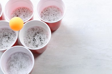 Plastic cups and ball on white table, above view with space for text. Beer pong game