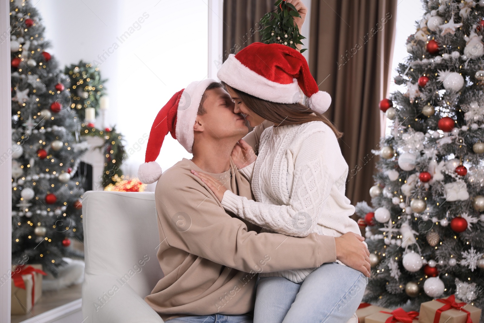 Photo of Couple kissing under mistletoe in room decorated for Christmas