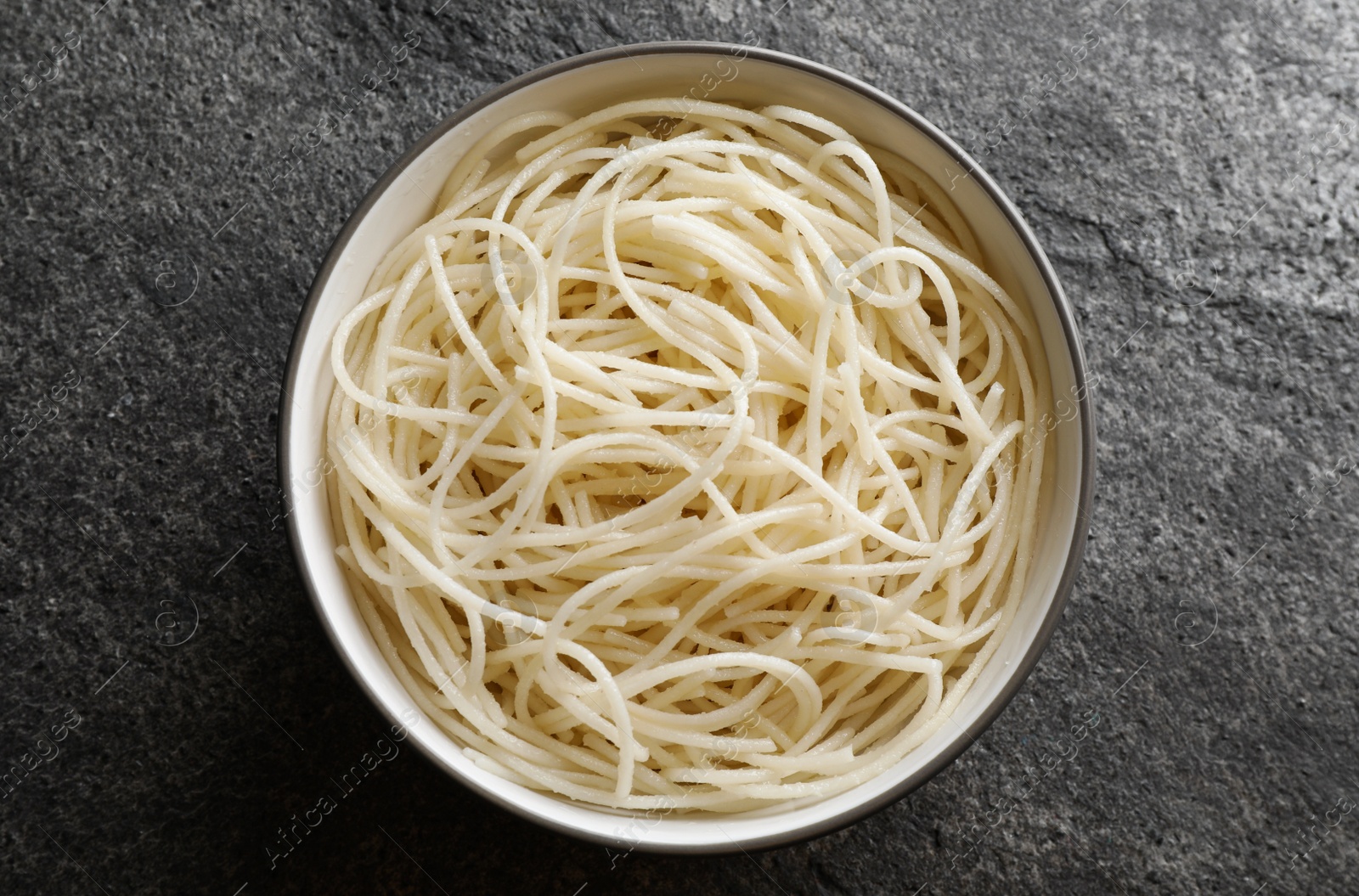 Photo of Bowl of tasty cooked rice noodles on grey table, top view