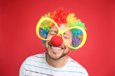 Funny man with large glasses, rainbow wig and clown nose on red background. April fool's day