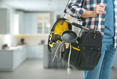 Image of Young plumber with tool bag in kitchen, closeup. Space for text