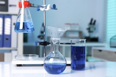 Photo of Laboratory analysis. Flasks and beaker with blue liquid on white table indoors