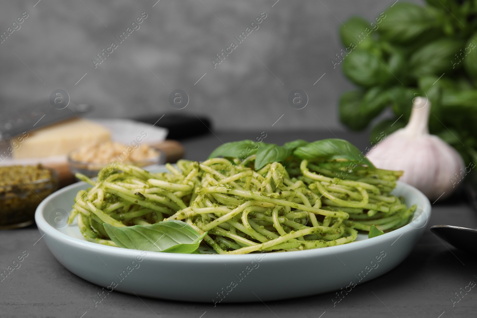 Photo of Delicious pasta with pesto sauce and basil on grey wooden table, closeup