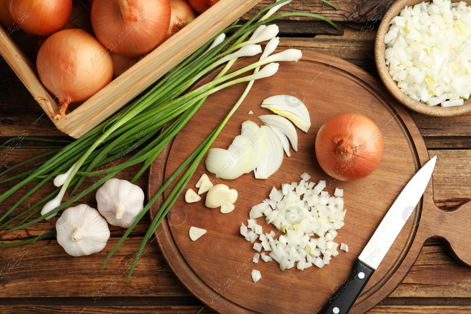Photo of Board with cut onion and garlic on wooden table, flat lay