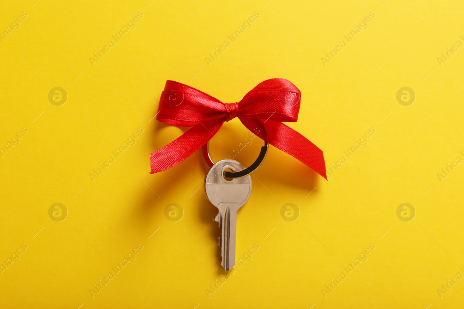 Photo of Key with red bow on yellow background, top view. Housewarming party