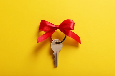 Photo of Key with red bow on yellow background, top view. Housewarming party