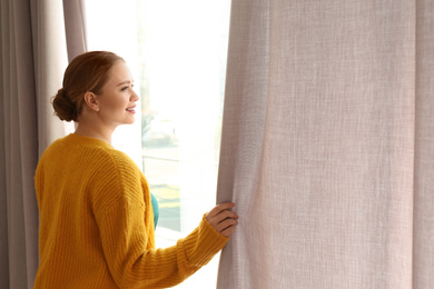 Woman opening window curtains at home in morning. Space for text