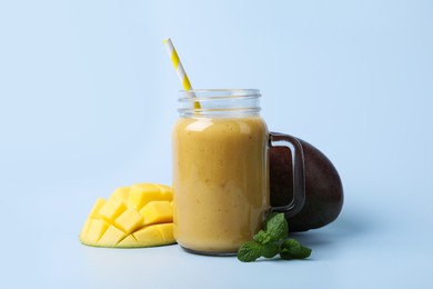 Mason jar with delicious fruit smoothie and fresh mango on light blue background