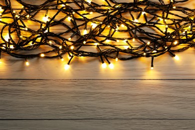 Photo of Glowing festive lights on wooden background, top view. Space for text
