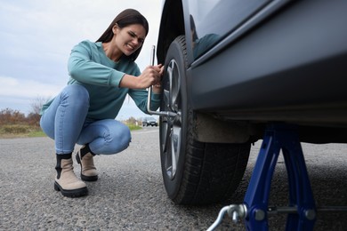 Young woman changing tire of car outdoors