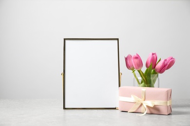 Image of Beautiful tulips, gift and blank photo frame on light table