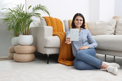 Young woman with greeting card on floor in living room
