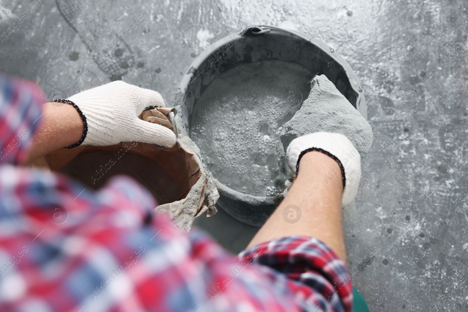 Photo of Worker with cement powder and trowel mixing concrete in bucket indoors, closeup