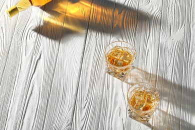 Photo of Whiskey with ice cubes in glasses on white wooden table, above view. Space for text