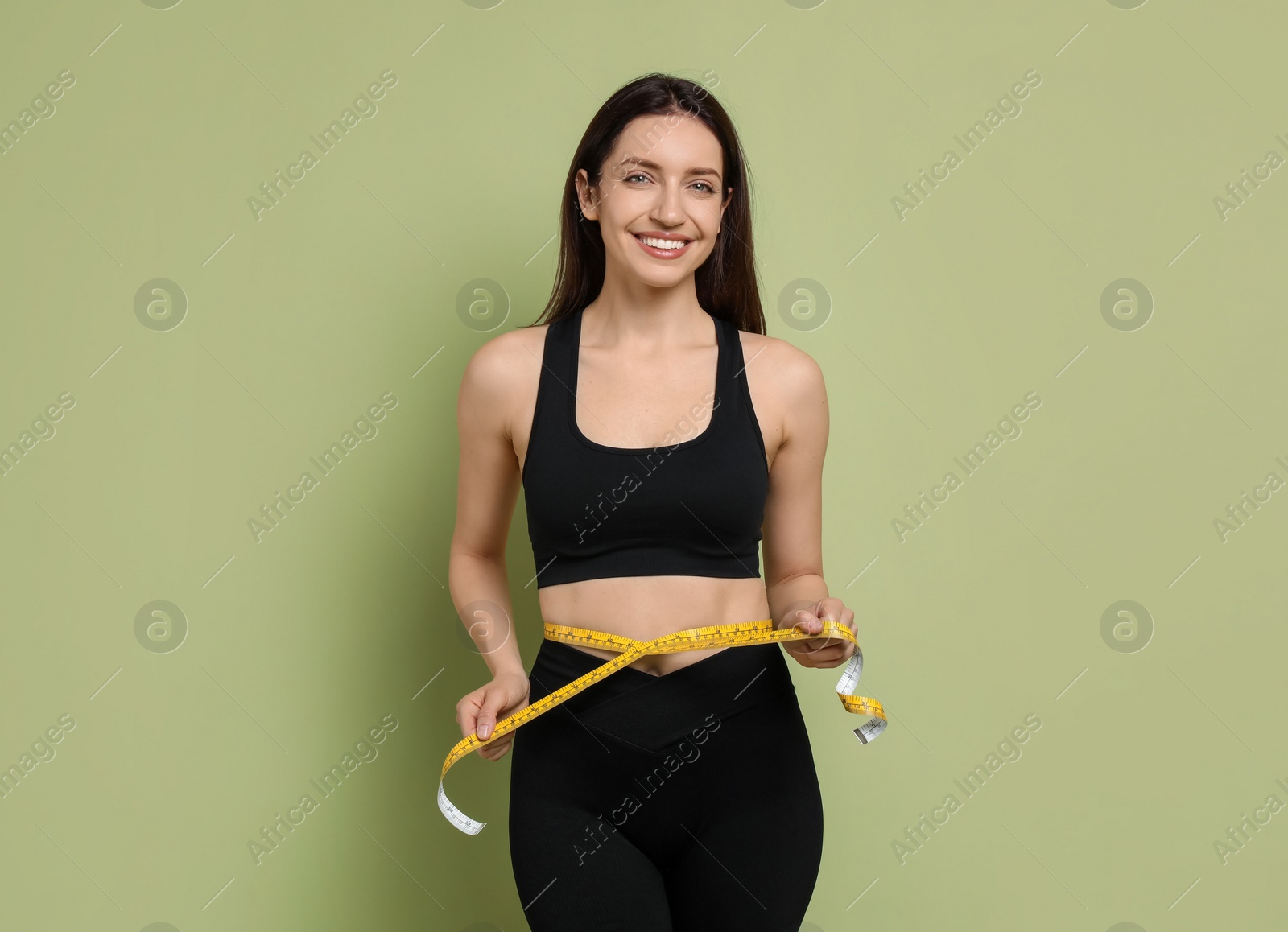 Photo of Happy young woman with measuring tape showing her slim body on green background