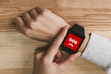 Woman using SOS function on smartwatch at wooden table, closeup