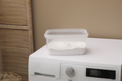 Plastic container with detergent powder on washing machine in laundry room