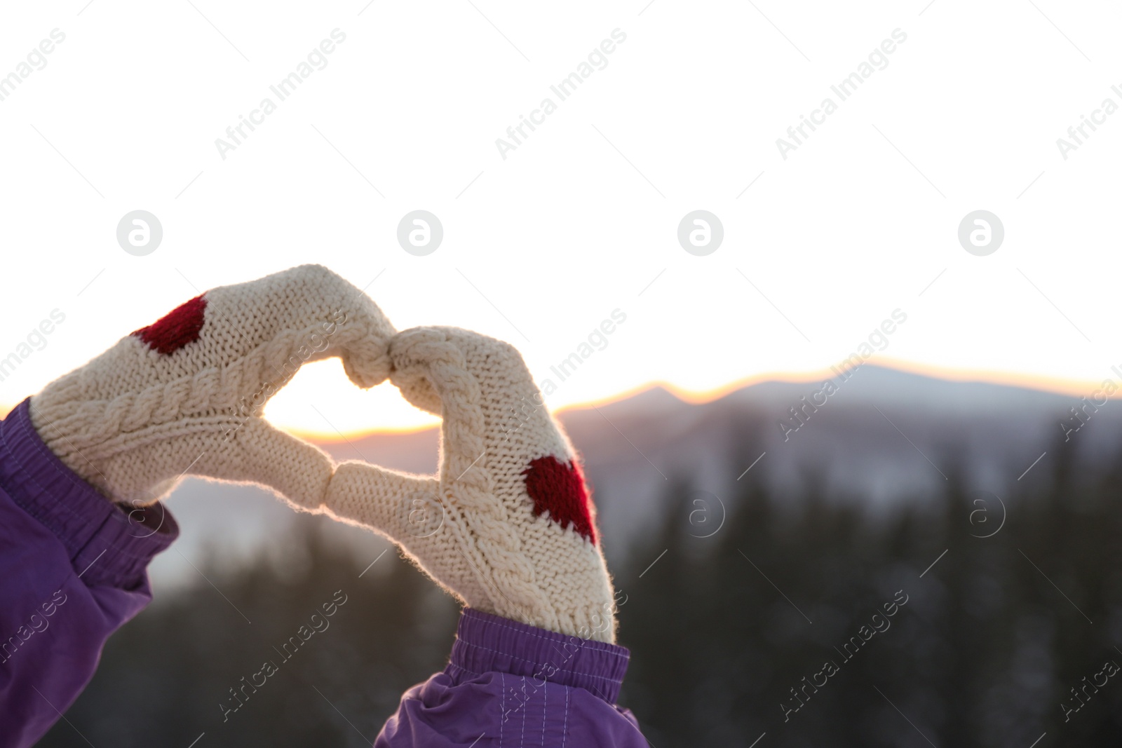 Photo of Woman making heart with her hands in mountains at sunset, closeup. Winter vacation