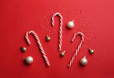 Photo of Candy canes and Christmas balls on red background, flat lay