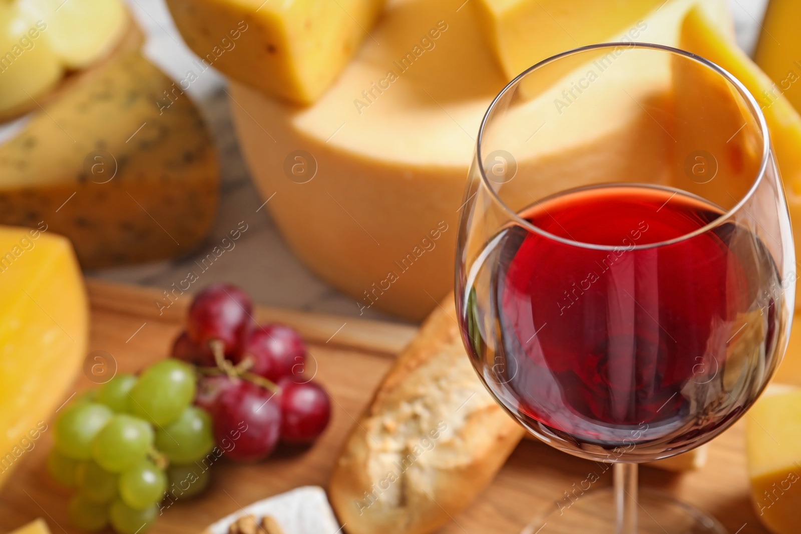 Photo of Glass of wine served with delicious cheese and snacks on table, closeup