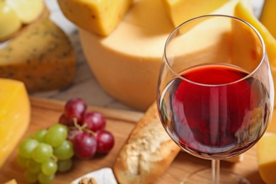 Photo of Glass of wine served with delicious cheese and snacks on table, closeup