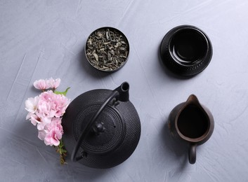 Beautiful set for traditional tea ceremony and sakura flowers on light grey table, flat lay