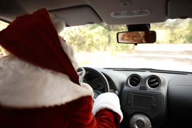Authentic Santa Claus looking at rear-view mirror of car