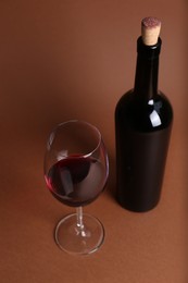 Photo of Glass and bottle of red wine on brown background