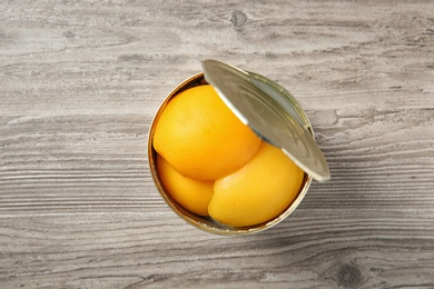 Photo of Open tin can of peaches on wooden background, top view