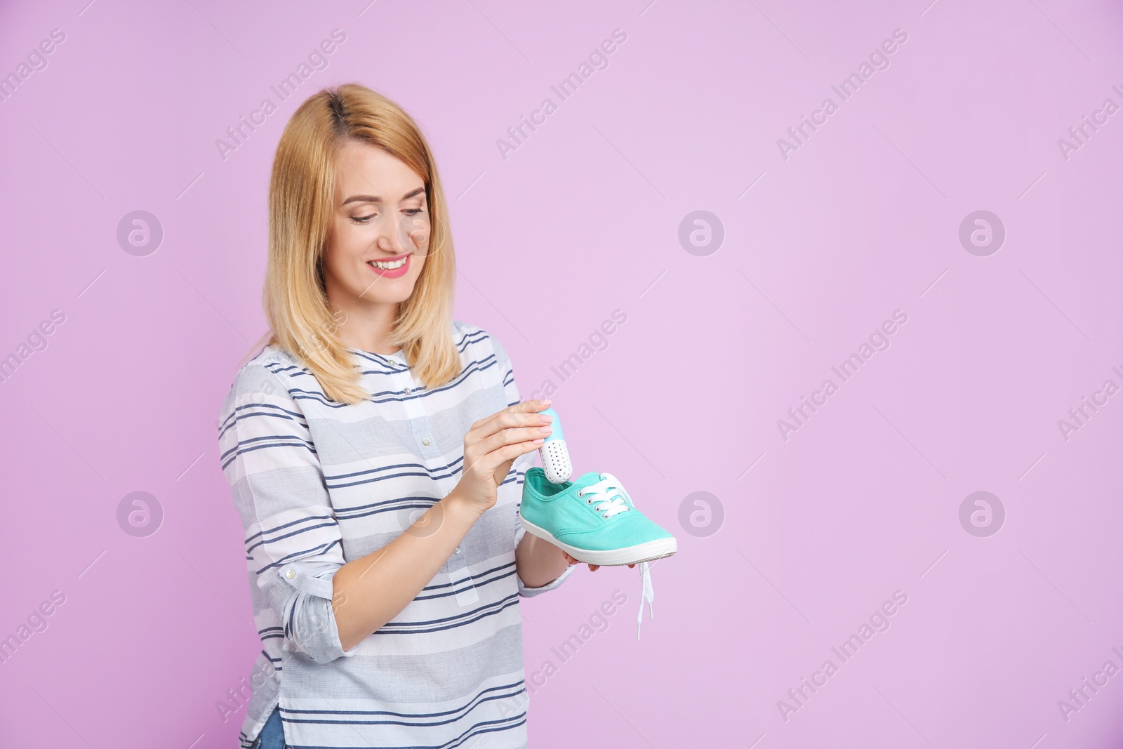 Photo of Young woman putting capsule air freshener in shoe on color background