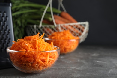 Glass bowl with grated carrot on grey table, closeup