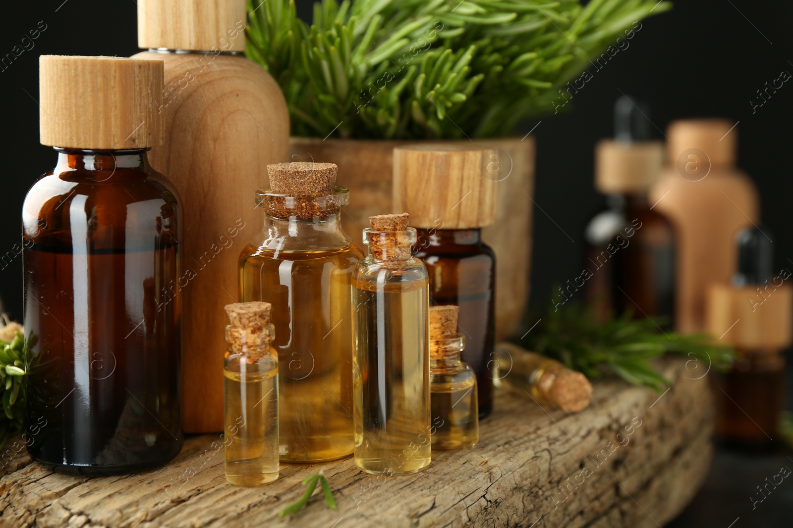 Photo of Essential oils in bottles, rosemary and wood on table against dark background, closeup