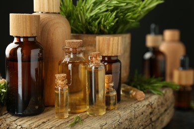 Essential oils in bottles, rosemary and wood on table against dark background, closeup